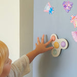 Child interacting with a colorful toy on a light gray wall with decorative stickers.