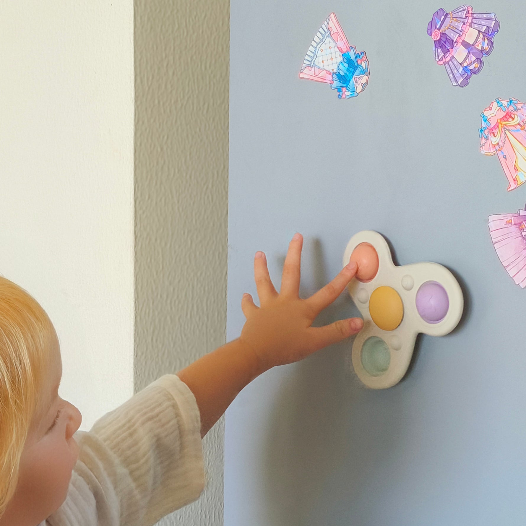 Child interacting with a colorful toy on a light gray wall with decorative stickers.