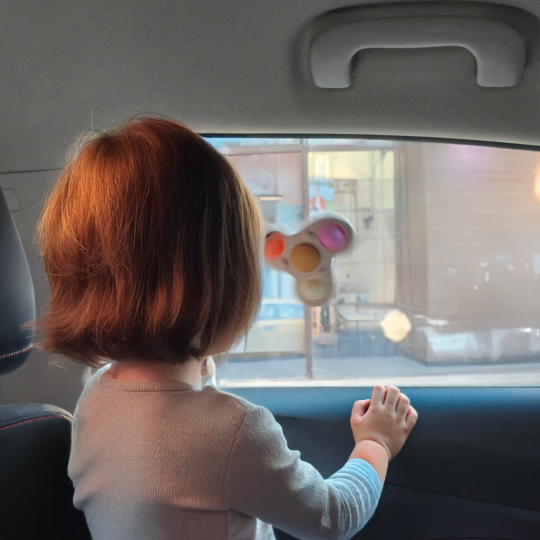 Child with red hair sitting in a car, looking out the window.