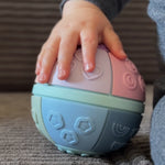 Child's hand holding a textured ball with geometric patterns on a carpeted floor.