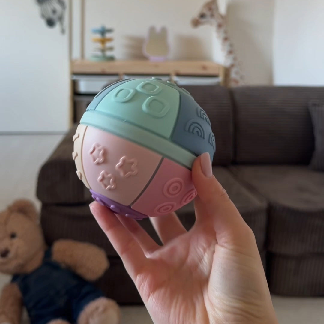 Colorful textured ball held in a hand with a living room background