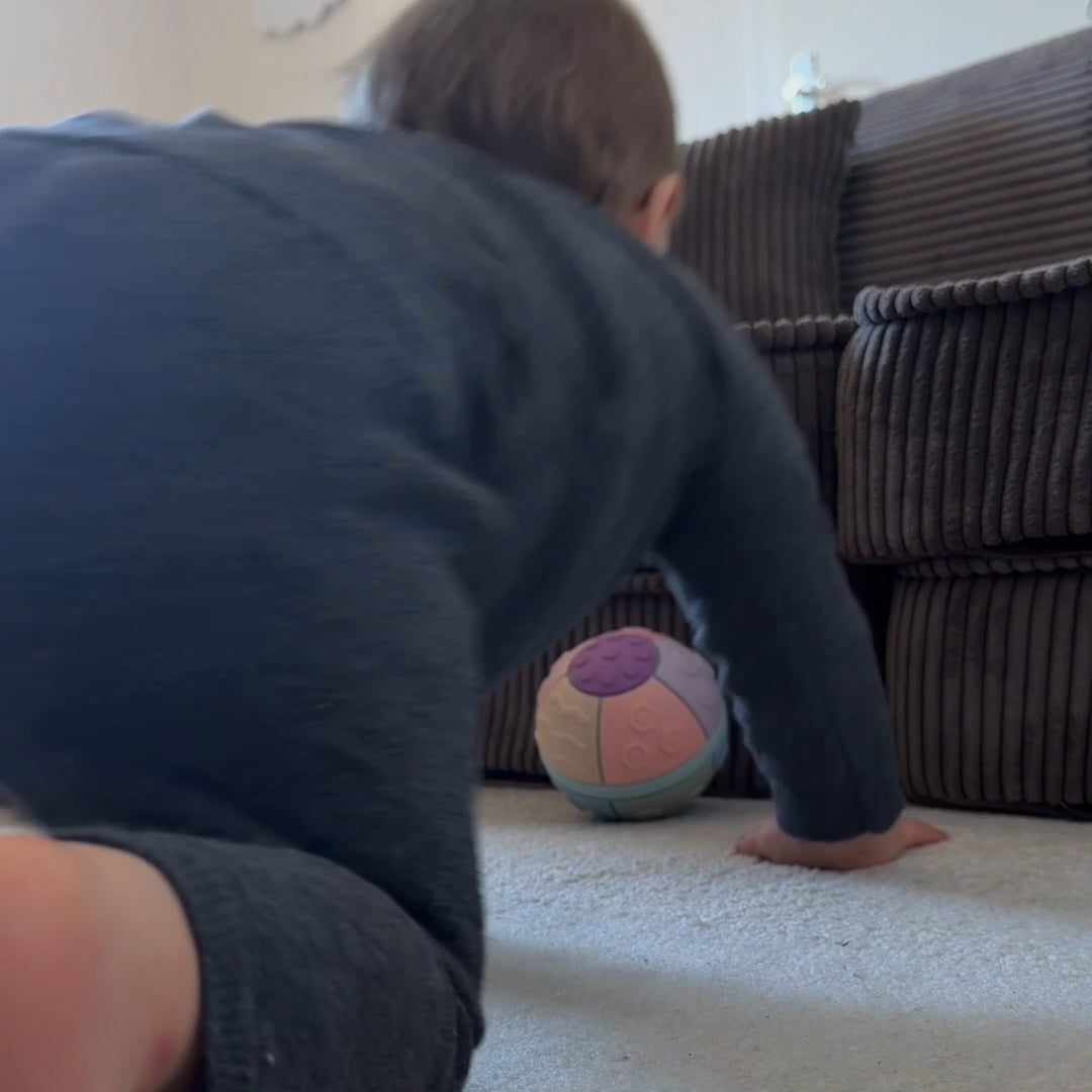 Child playing with a colorful ball on a carpeted floor next to a brown couch.