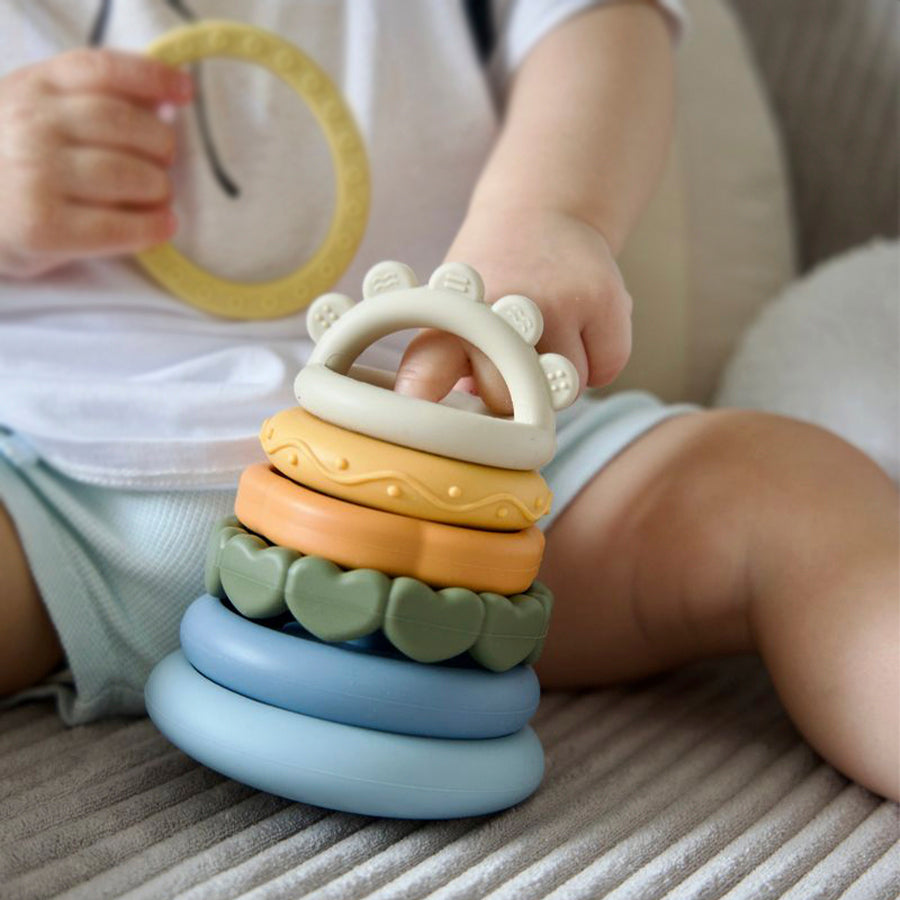Child playing with a stack of colorful baby toys on a soft surface 