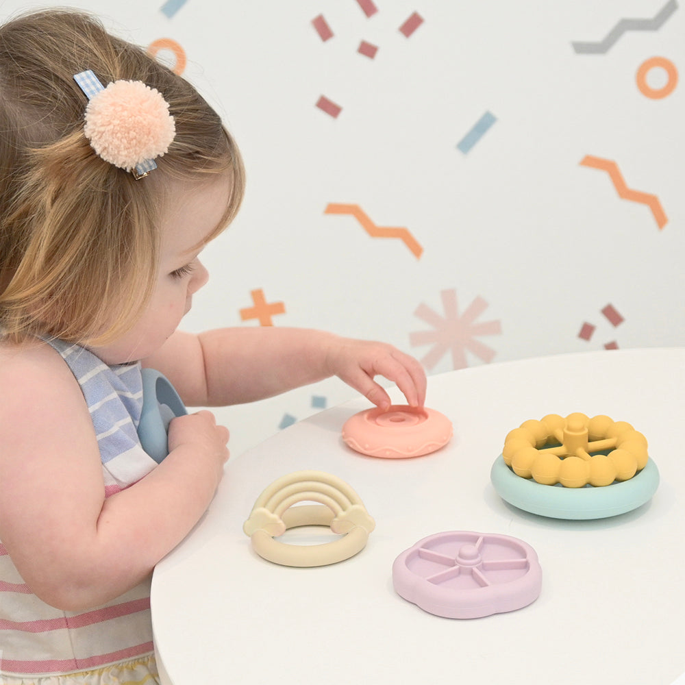 Child playing with colorful silicone teething rings on a white surface. 