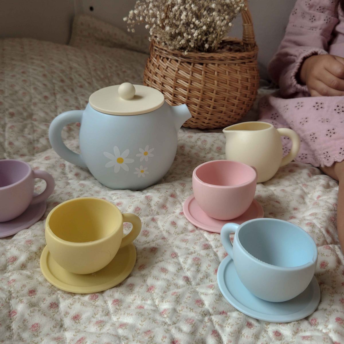 Set of pastel-colored ceramic tea sets on a floral-patterned surface.