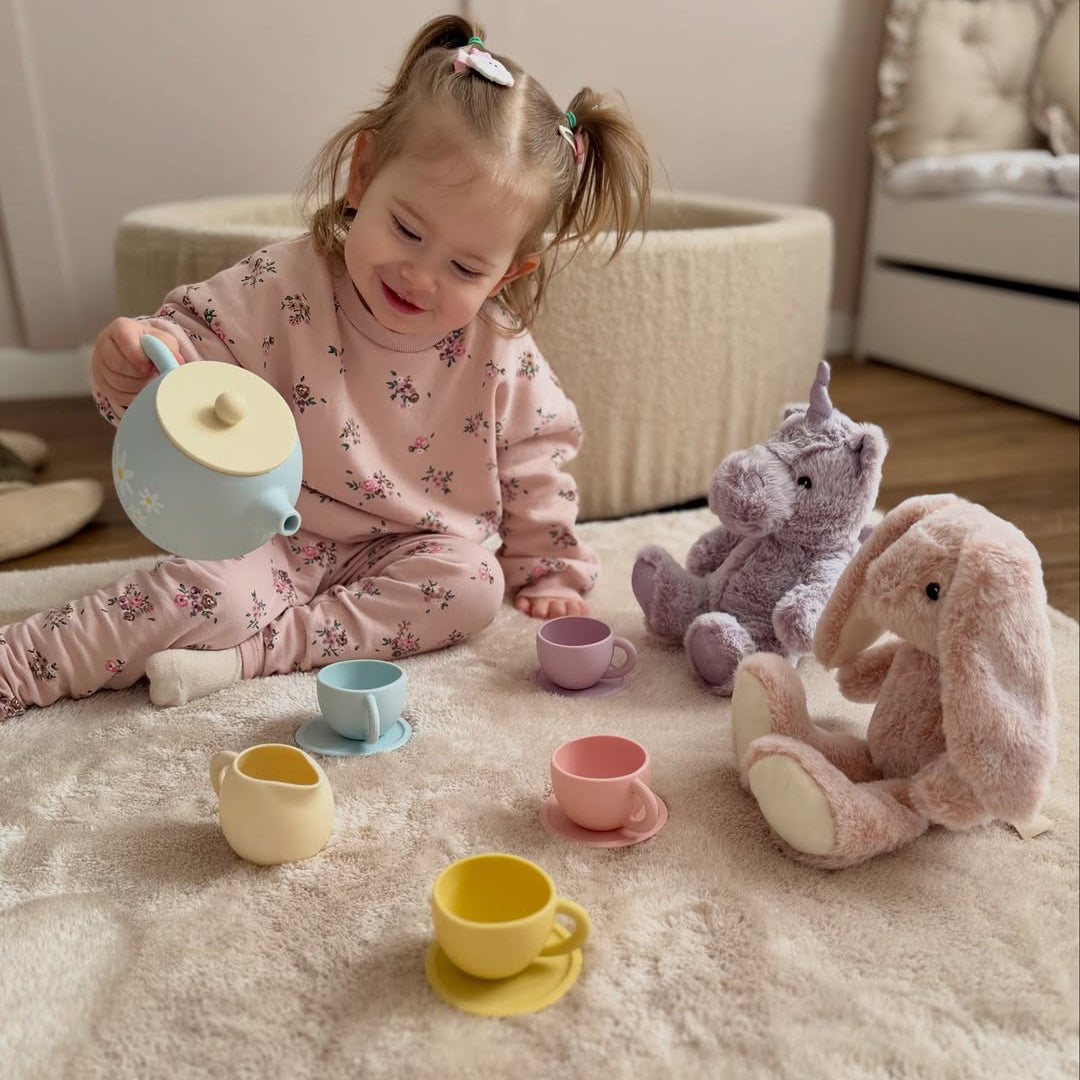 Child playing with toy tea set and plush toys on a carpeted floor.