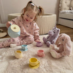 Child playing with toy tea set and plush toys on a carpeted floor.